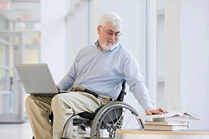 Business And Occupation Prints: University professor with Muscular Dystrophy reading a book and using a laptop