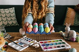 Prepare Prints: Unrecognizable female in sweater demonstrating carton with set of painted Easter eggs while sitting on sofa