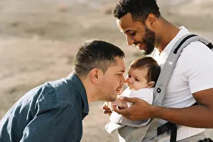 Diverse Prints: Side view of black casual with male boyfriend holding little calm baby in grey carrier while standing on nature