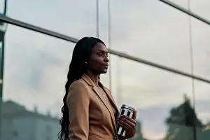 Relaxed Prints: side view of a black woman wearing a brown suit holding a laptop and a container of coffee walking next to a building