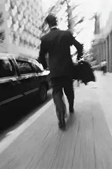 Business Attire Prints: Back View of Businessman Walking On Street Carrying Briefcase