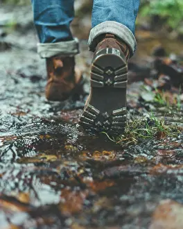 Anonymous Prints: Back view of crop male traveler in jeans and brown boots walking on wet trail in autumn forest