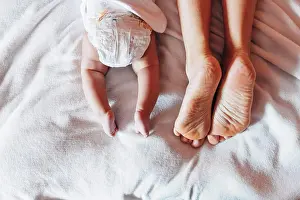 Anonymous Prints: Top view of crop newborn baby in diaper lying on bed with mother in house