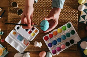 Anonymous Prints: From above top view of cropped unrecognizable person in sweater covering fresh chicken eggs with blue paint while