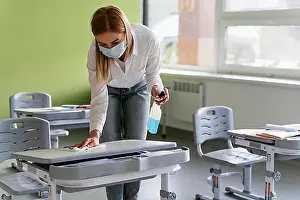 Vegetables Prints: front view female teacher disinfecting school benches classroom. High resolution photo