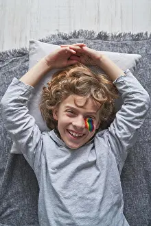 Cheerful Prints: Top view of happy boy with rainbow under eye lying on blanket and pillow