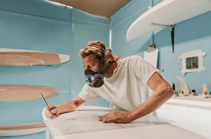 Anonymous Prints: Side view of male in breather holding pencil and measuring surf board in workplace