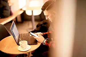 Networks Prints: View from above of a man in a red plaid shirt using his phone and laptop computer at a cafe