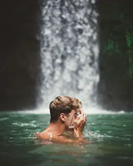 Freedom Prints: Side view of man washing face while swimming in clear water of lake with waterfall on background