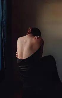 Lonely Prints: Back view of sad woman bent forward with back exposed in a dark room