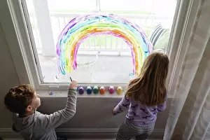 Sweater Prints: top down view of siblings painting rainbow on living room window
