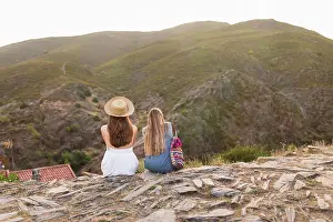 Edge Prints: Back view of two tourists women sitting together on mountain edge