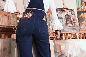 Talent Prints: Back view of woman with brushes in pockets standing at paintings in workshop