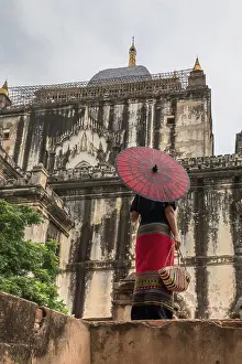 Anonymous Prints: From below back view of woman in long dress holding traditional Burmese red umbrella