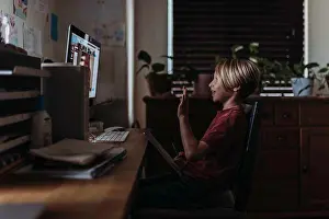 Electronics Prints: Side view of young boy waving to friends on video chat