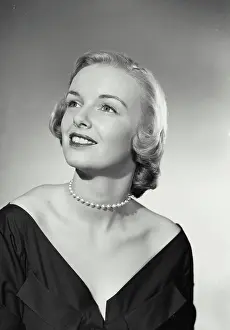 Gown Prints: Vintage Photograph. Smiling blonde woman wearing black evening gown and pearl necklace looking up and off camera
