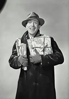 One Mid Adult Man Only Prints: Vintage Photograph. Smiling man wearing hat and winter coat dusted with snow holding wrapped holiday presents