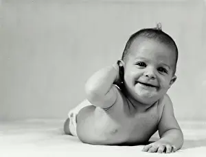 Vintage Photograph. Baby crawling with hand behind head smiling