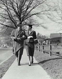 Husband Prints: Vintage Photograph. Well dressed man and woman walking arm in arm down sidewalk with bare tree in background Frame 1