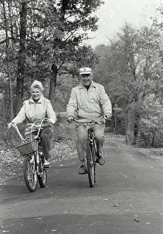 Cycling Prints: Vintage Photograph. Elderly couple riding bicycles down autumn road