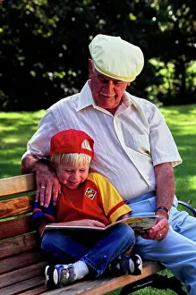 Grandfather Prints: Vintage Photograph. Grandfather and grandson enjoying a storybook together in the park
