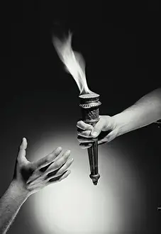 Finger Prints: Vintage Photograph. Hand passing torch with flame to hand reaching up from bottom of frame with dark background