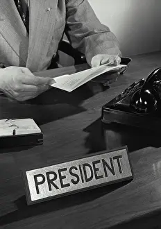 Identity Prints: Vintage Photograph. Hands holding stack of papers at desk with telephone and president title card