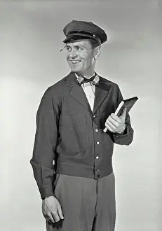 Note Pad Prints: Vintage Photograph. Mailman in uniform with pencil stuck in hat brim holding up notepad smiling