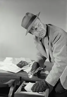 Criminal Prints: Vintage Photograph. Man dressed as thief rummaging through desk drawer with flashlight in hand