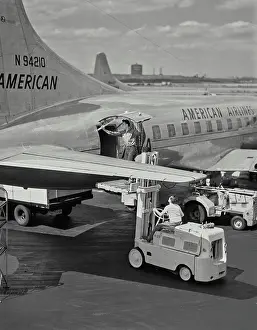Planes Prints: Vintage photograph. Man opening cargo door on American Airlines plane while standing on forklift pallet