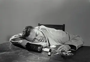 Smoking Prints: Vintage Photograph. Man passed out drunk on table with empty liquor bottle and ashtray filled with cigarettes