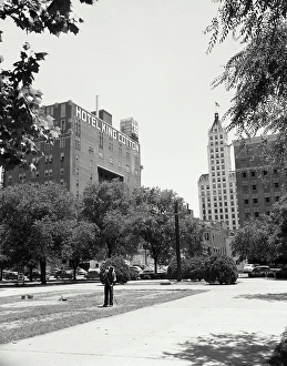 Vintage Photograph. Man raking leaves in city park showing the skyline of Memphis