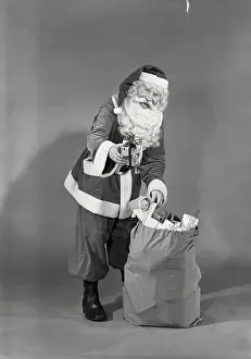 Suit Prints: Vintage photograph. Man in Santa Claus costume grabbing Christmas toys from sack