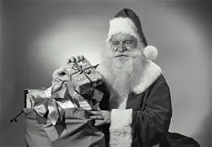Outfit Prints: Vintage Photograph. Man in Santa Claus outfit takes gifts out of sack as he smiles