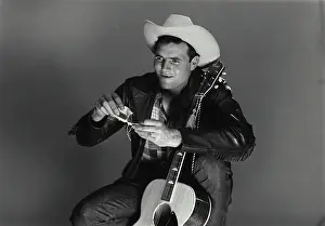 Smoking Prints: Vintage Photograph. Man sits with guitar as he rolls up a ciggarette
