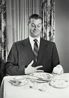 Knife Prints: Vintage photograph. Man at table holding full stomach with empty plates
