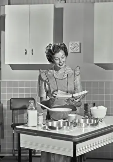 Flour Prints: Vintage photograph. Mid adult woman reading a cookbook and smiling