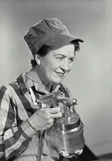 Fingers Prints: Vintage photograph. Middle aged woman dressed in work uniform holding paint sprayer with fingers on trigger