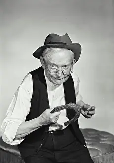 Staring Prints: Vintage Photograph. Old man with glasses wearing hat and wool vest about to throw horseshoe
