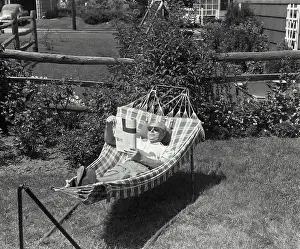 Newspaper Prints: Vintage Photograph. An older man laying in a hammock wearing sunglasses reading a magazine