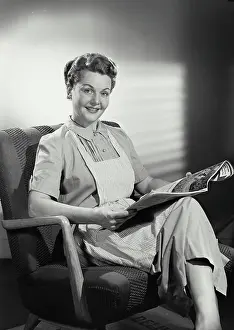 Newspaper Prints: Vintage photograph. Portrait of woman in striped apron sitting and reading newspaper