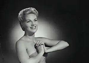 Gown Prints: Vintage Photograph. Smiling blonde woman with hair up and low cut gown clasping hands together in front of chest