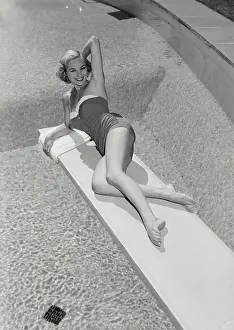 Activewear Prints: Vintage Photograph. Smiling blonde woman wearing bathing suit lying on diving board over swimming pool