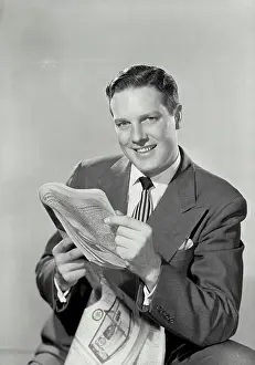 Bill Prints: Vintage Photograph. Smiling brunette man in suit holding up newspaper