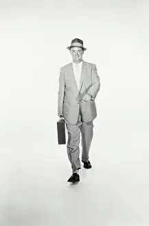 Briefcase Prints: Vintage Photograph. A studio shot of a man wearing a suit and holding a briefcase walking towards the camera