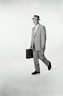 Business Attire Prints: Vintage Photograph. A studio shot of a man wearing a suit and holding a briefcase walking across frame