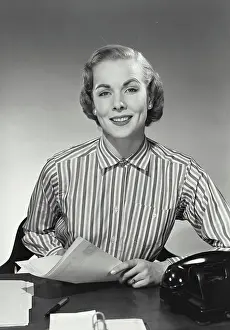 One Young Woman Only Prints: Vintage Photograph. Woman in striped collared blouse holding papers at desk and smiling