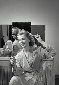 Vanity Prints: Vintage Photograph. Woman wearing robe combing hair holding up mirror with vanity table in background