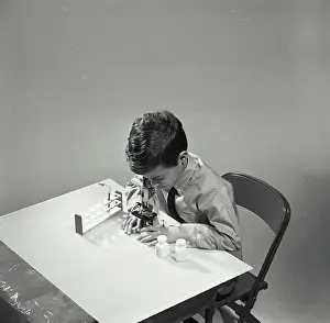 Academic Prints: Vintage Photograph. Young boy looking through microscope on table against white backdrop