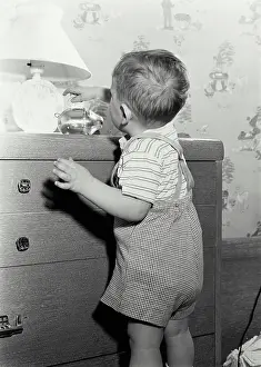 Household Prints: Vintage Photograph. Young boy placing coin in piggy bank